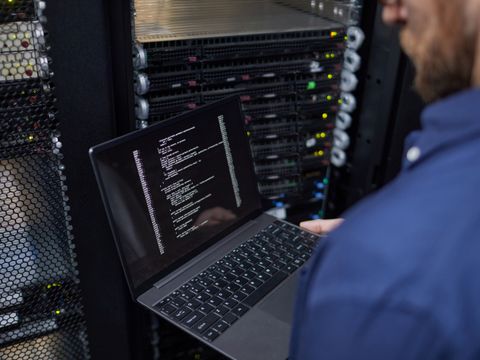 Techniker steht im Serverraum mit Laptop in der Hand.