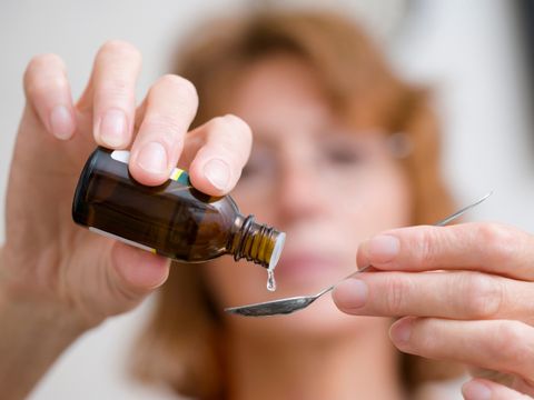 Frau tröpfelt Medizin in einen Teelöffel.