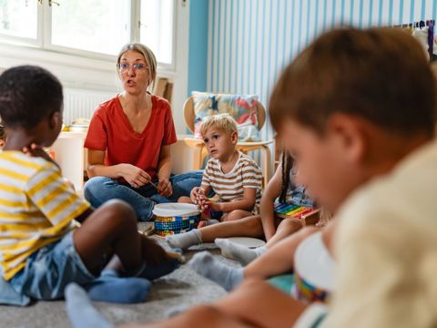Erzieherin sitzt mit kleinen Kindern im Kreis.