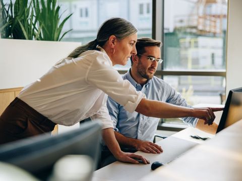 Frau zeigt in einem Büro einem Mann etwas auf dem Computerbildschirm.